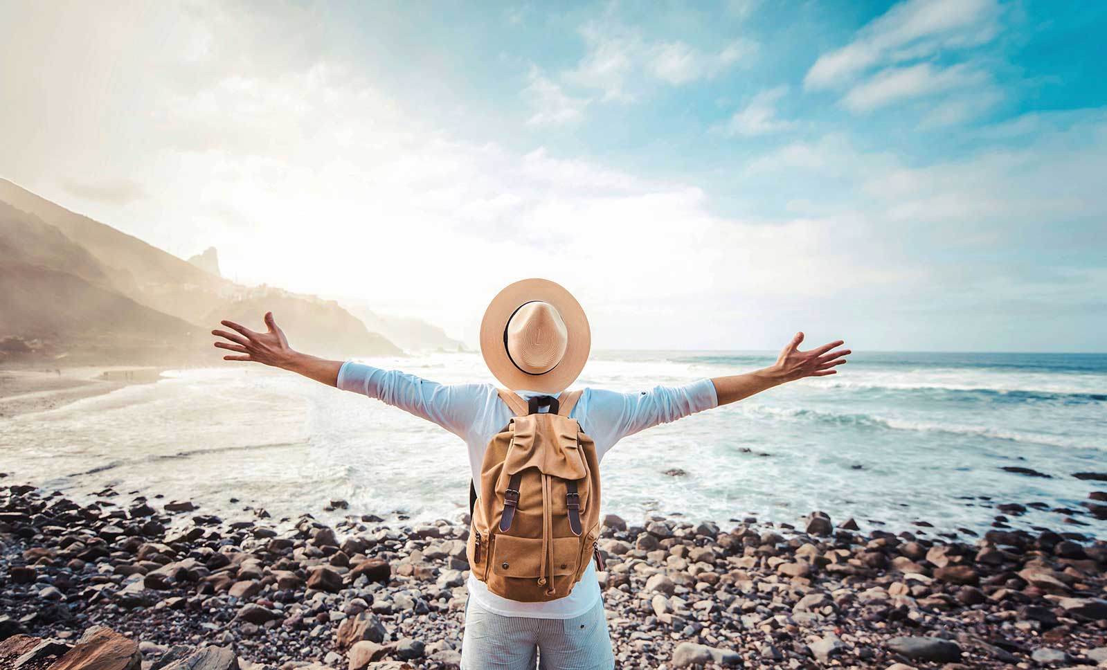 AdobeStock_558165368-(1) Happy tourist with backpack enjoying freedom raising arms up