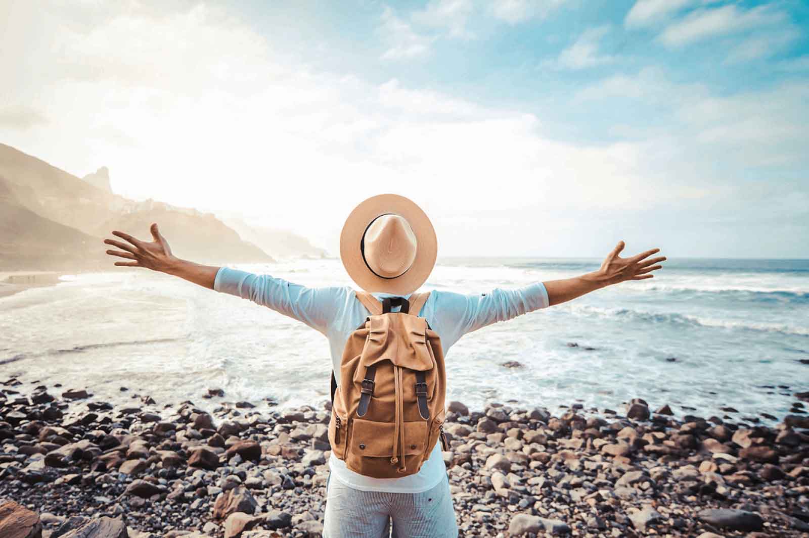 Happy tourist with backpack enjoying freedom raising arms up