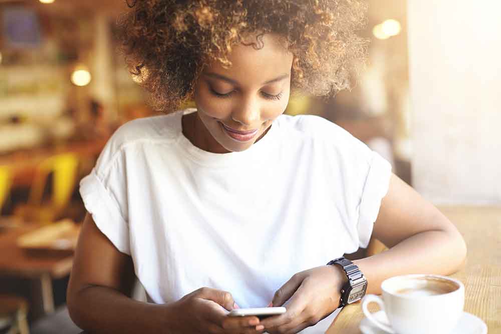 AdobeStock_121012784 Image of a woman looking at her phone in a cafe.