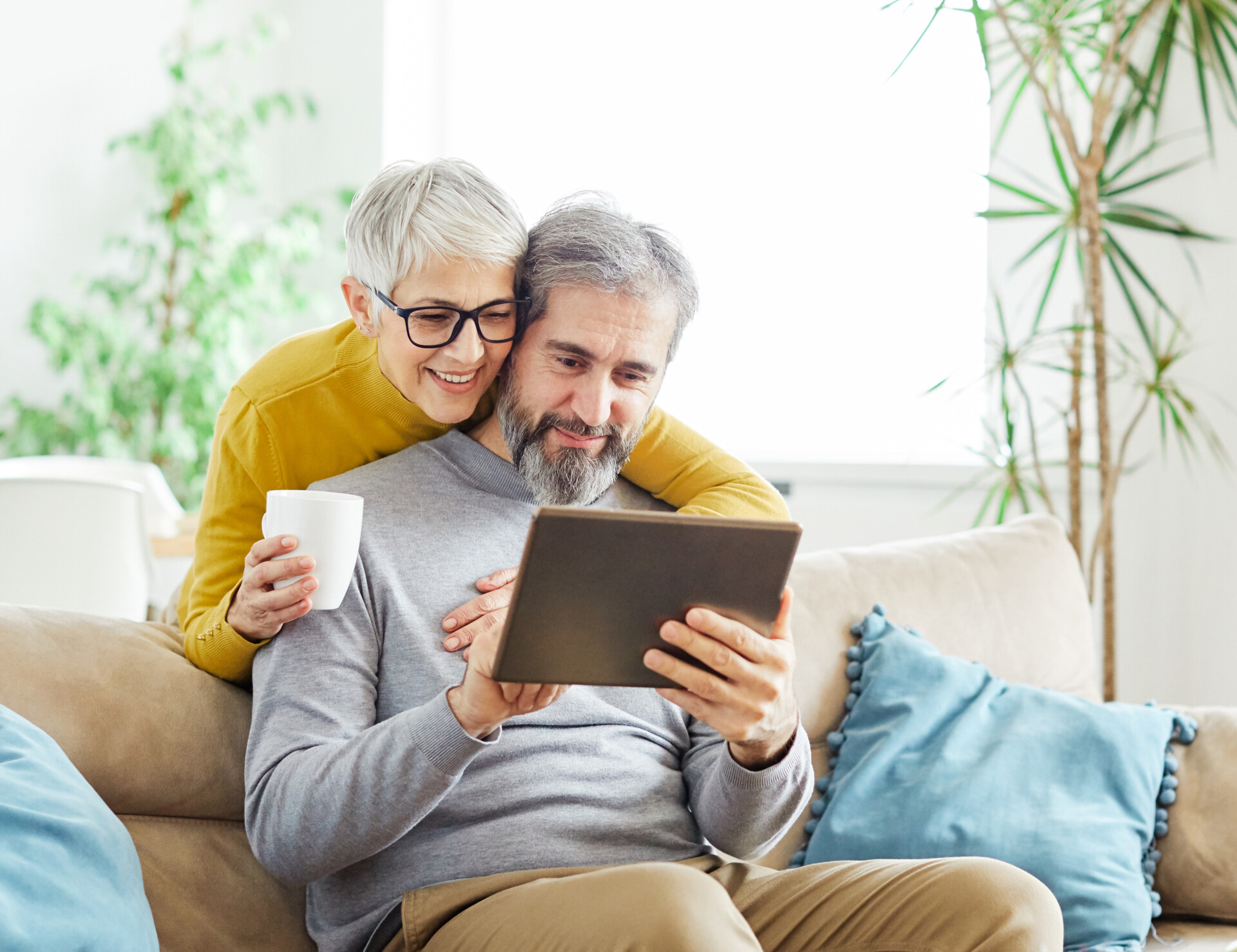 Portrait of a lovely senior mature couple together holding a tablet on sofa at home