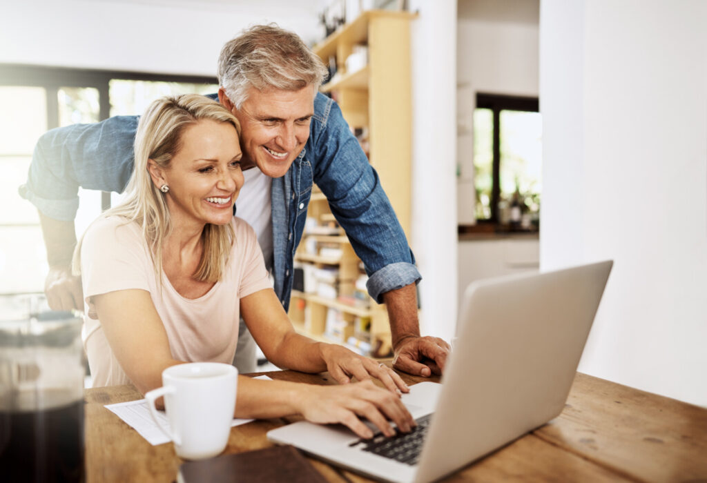 Happy, smiling and mature couple using a laptop together at home. Cheerful Middle aged partners working as a team online.