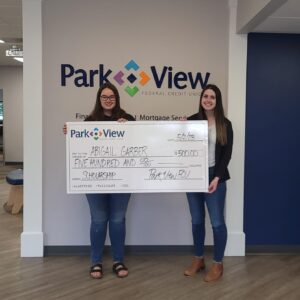 Abigail Garber, 2023 Scholarship Winner, holds a giant, oversized check with Harmony Square Park View FCU Branch Manager Jordan Tyler.
