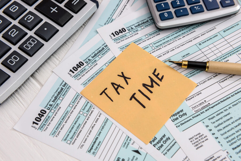 Tax forms and a sticky note that states "tax time" on a table.