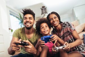 Parents and two children gathered around a gaming console, laughing and enjoying a video game together, protecting child from video game scam.
