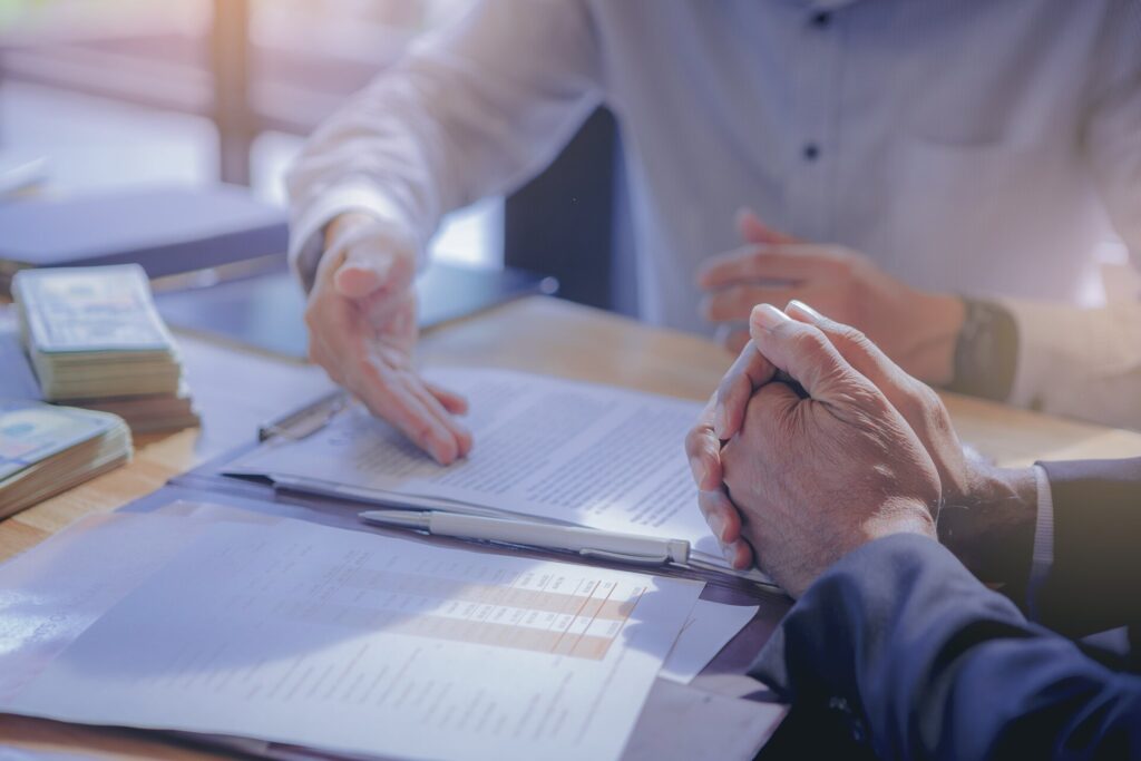 Two business people sitting at a table with papers and money, discussing financial documents and discussing the 5 C's of Credit for small business financing.