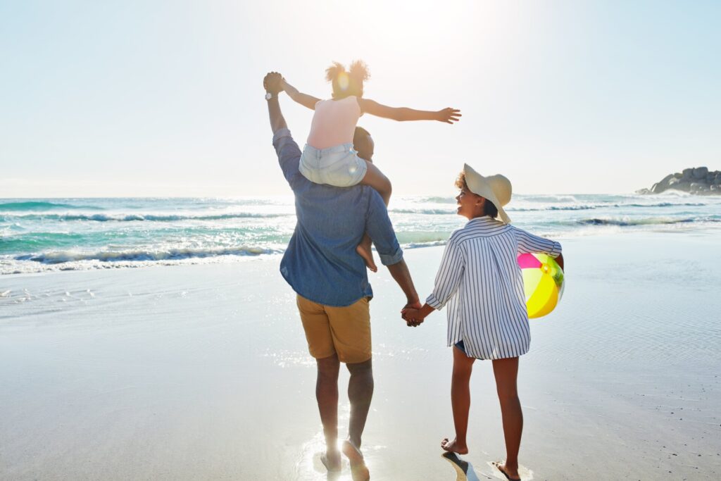 A family enjoying a beach stroll, holding hands, while the sun sets. Thinking of summer savings tips.