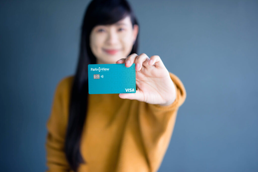 "A young woman holding a Park View Visa credit card, smiling and presenting it towards the camera.