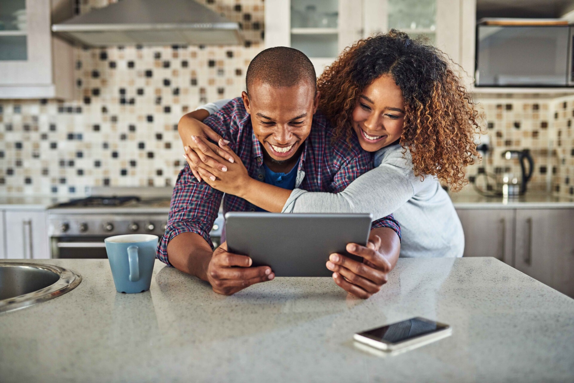 AdobeStock_498696968 (2) A man and woman in a kitchen are reviewing their online banking details on a tablet together.