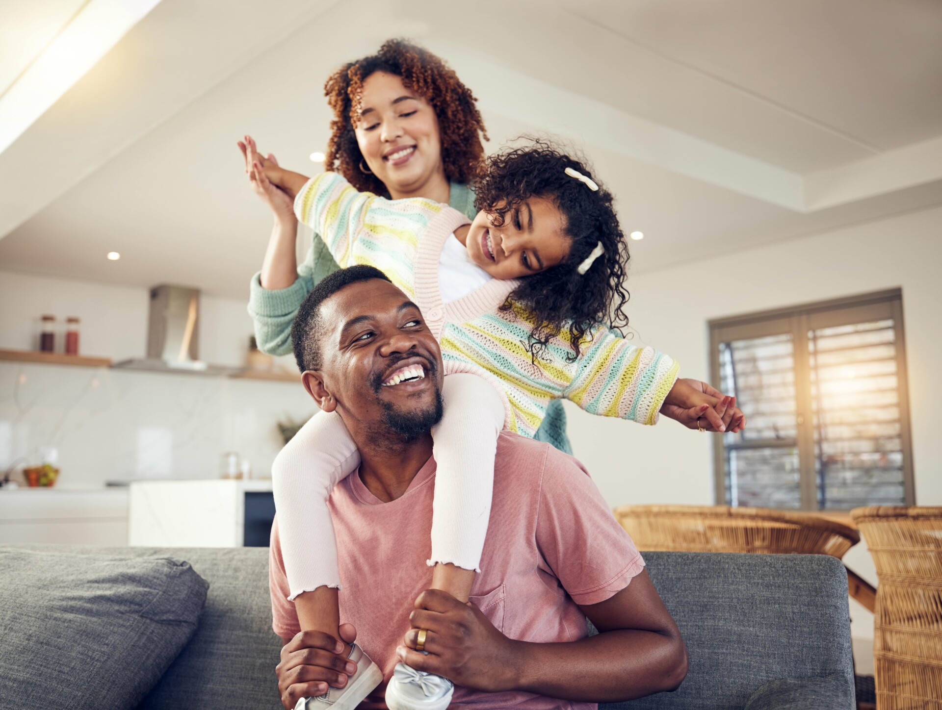 A man, woman, and their daughter relax on a couch, sharing smiles and laughter, highlighting the importance of health savings.