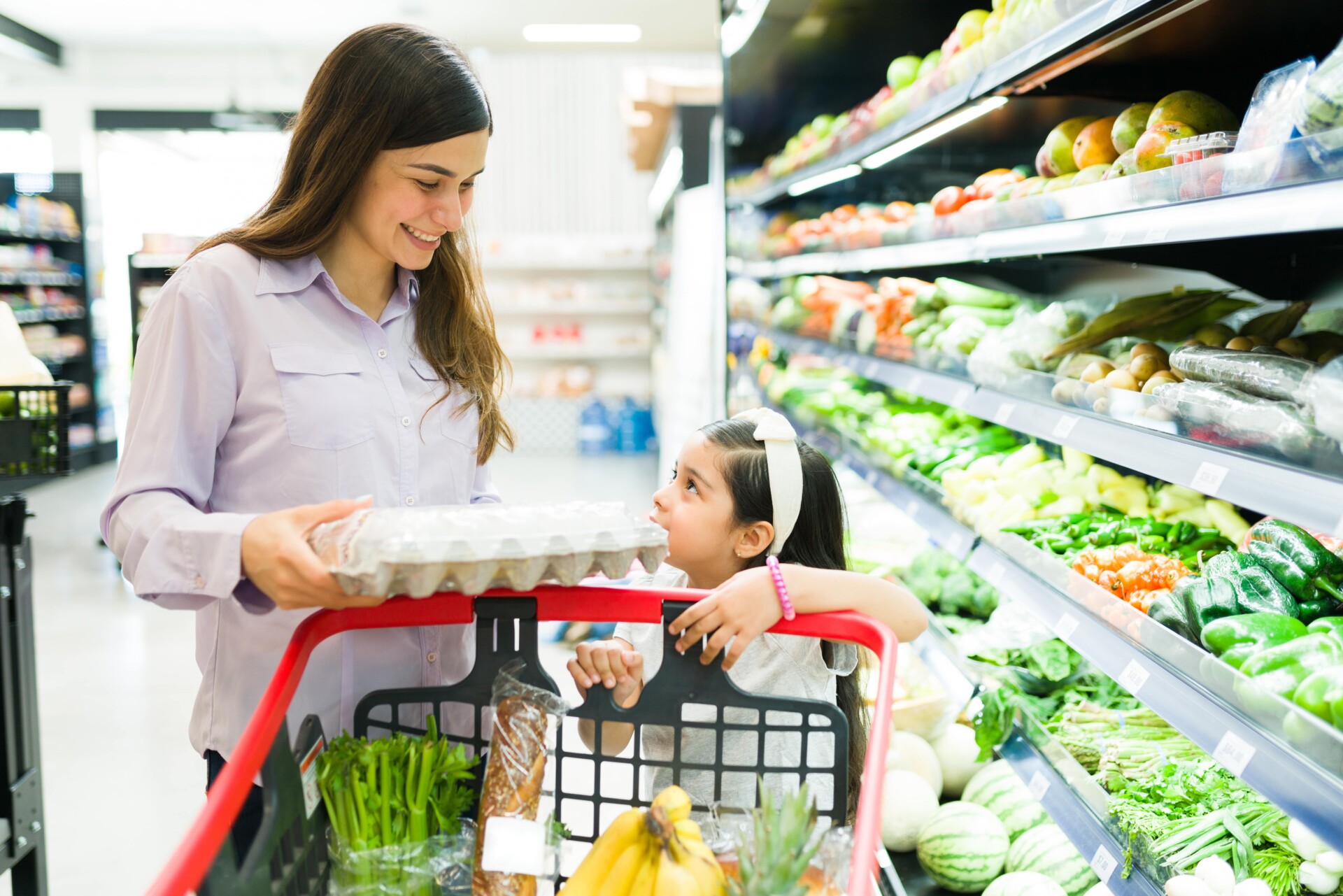A woman and her child browse the grocery store, looking at products while managing their shopping list together.