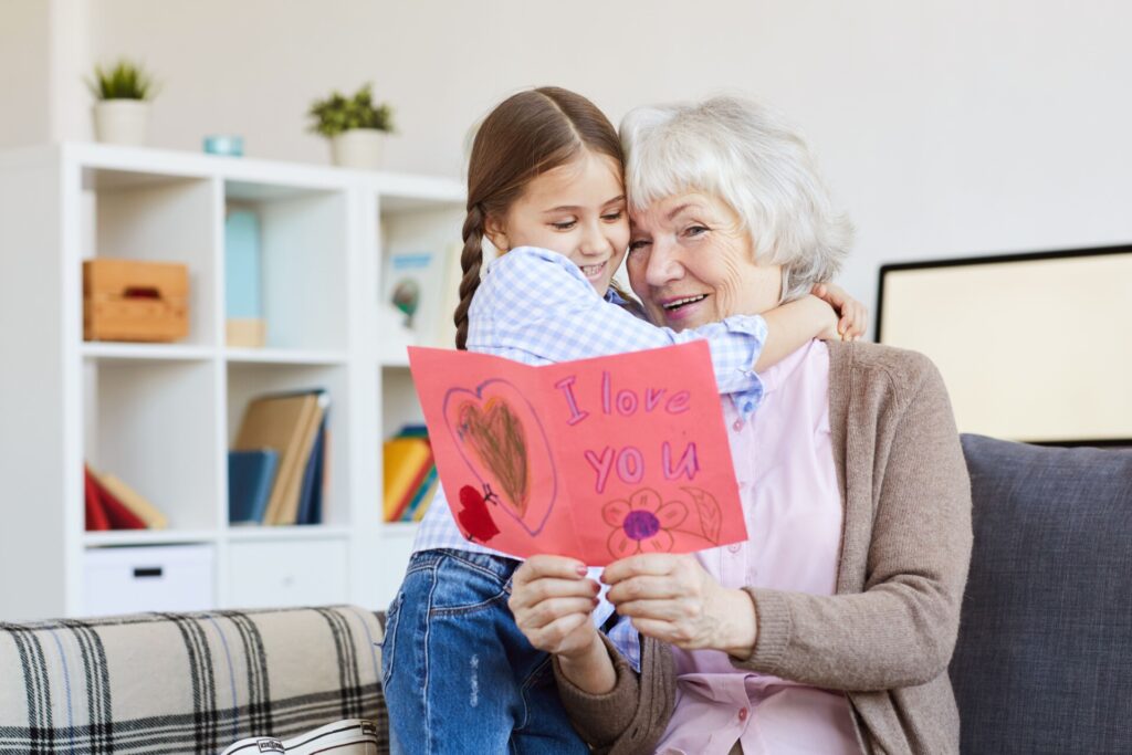 Granddaughter hugs her grandmother while giving a handmade Valentine’s card, a budget-friendly Valentine’s Day idea.