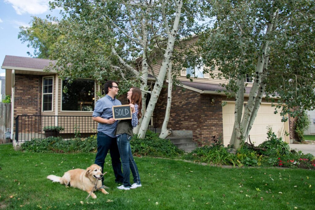 A couple joyfully stands in front of their new home, celebrating their achievement as first-time homebuyers.