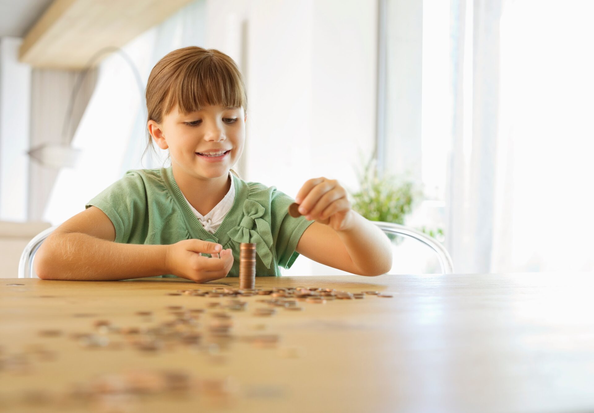 A young girl sits at a table, counting coins, representing her youth savings account and learning about saving money.