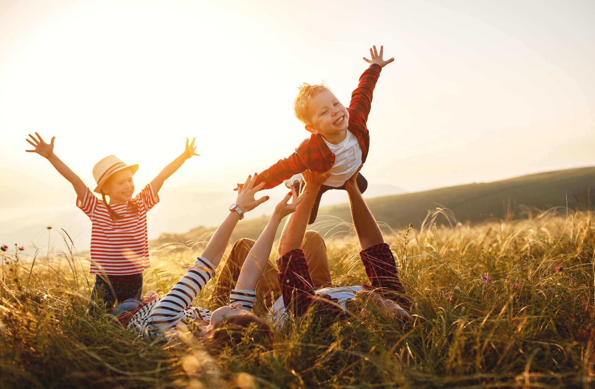 A family laughs and plays on the grass, creating happy memories at sunset.