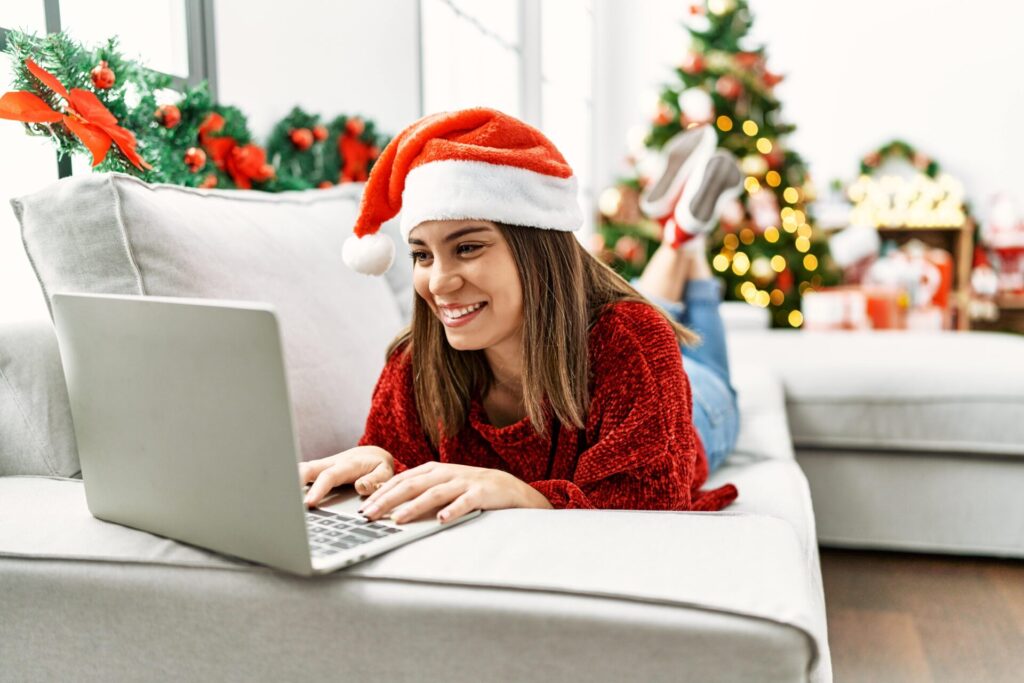 A woman in a festive Santa hat uses her laptop, learning about how to save $1000 for the holidays.