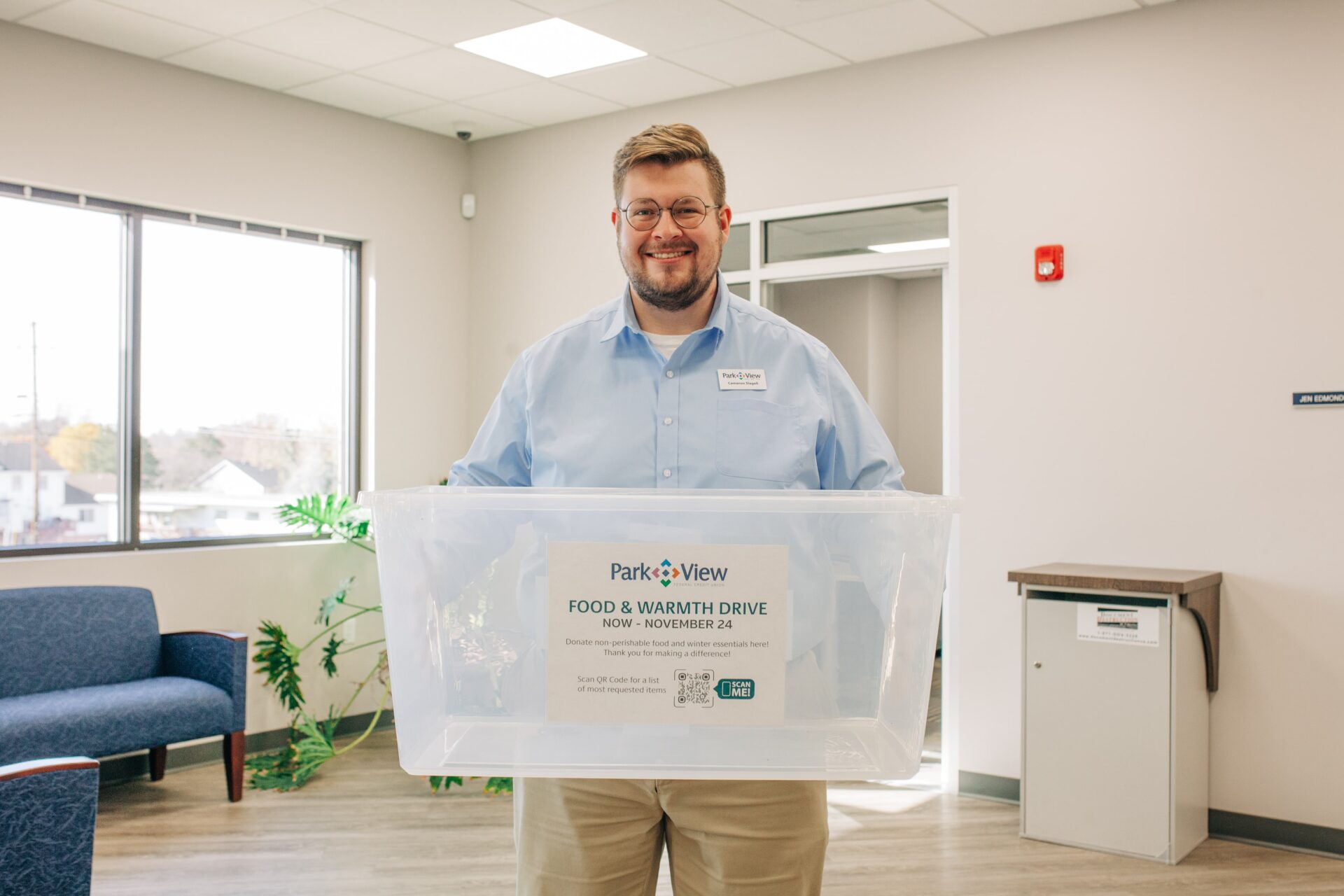 A male Park View employee holds a clear plastic bin for a food and winter supply drive.