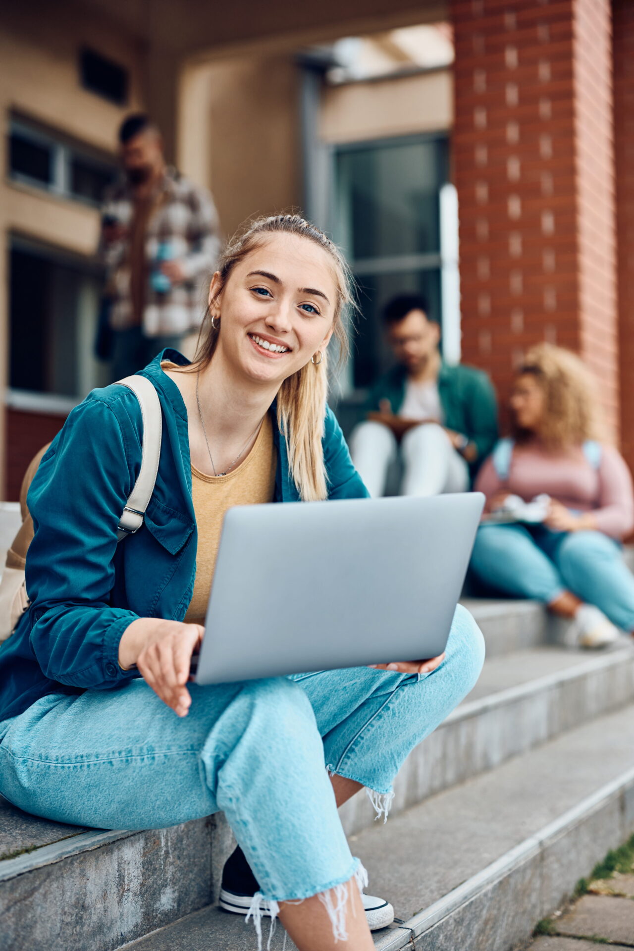 Downloaded Happy female student using laptop at campus and looking at camera.