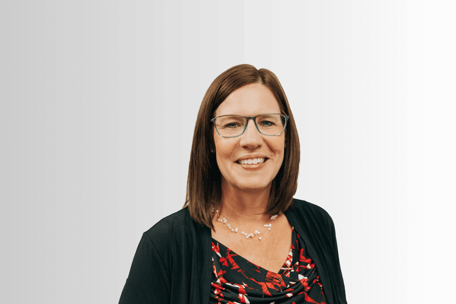Professional headshot of a smiling woman with glasses and shoulder-length brown hair, wearing a black cardigan and red floral blouse.