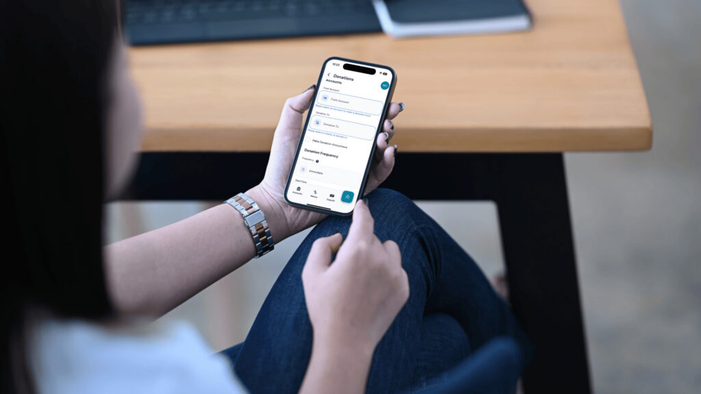 A woman uses her mobile phone to view her bank account, utilizing a donation tool for her charitable giving.