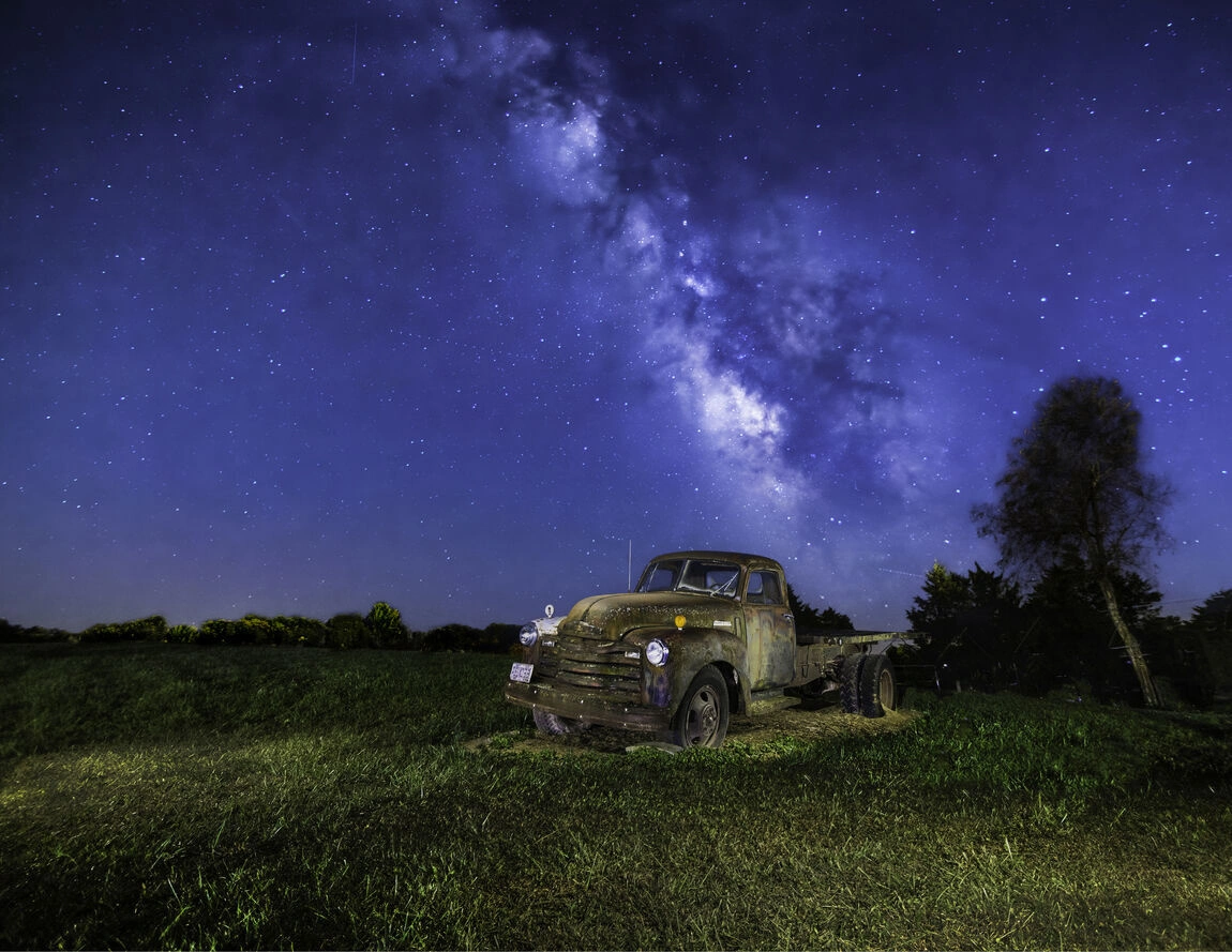 A stunning view of the Milky Way galaxy shining brightly above a parked truck in a dark, starry night sky.
