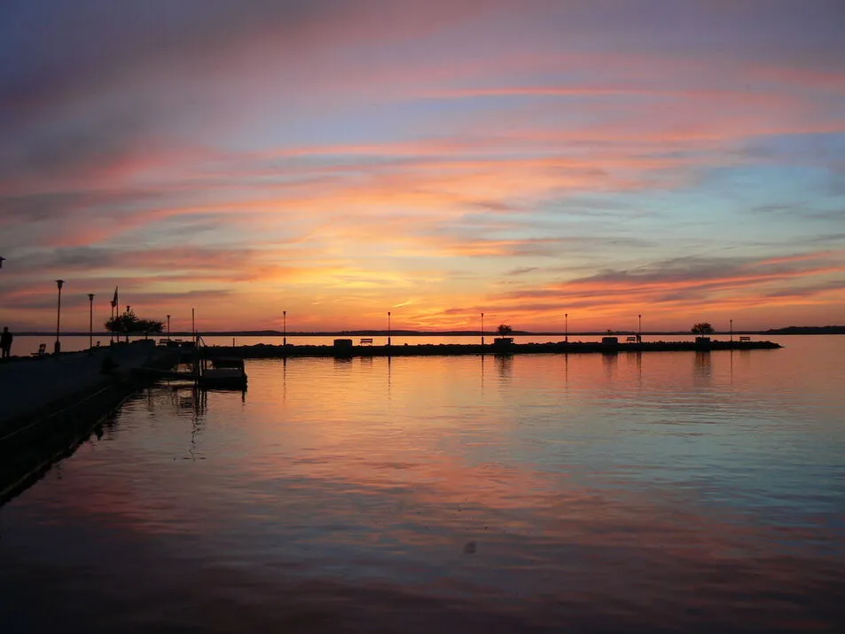A peaceful boat resting on the dock as the sun sets, casting warm colors across the sky and water.