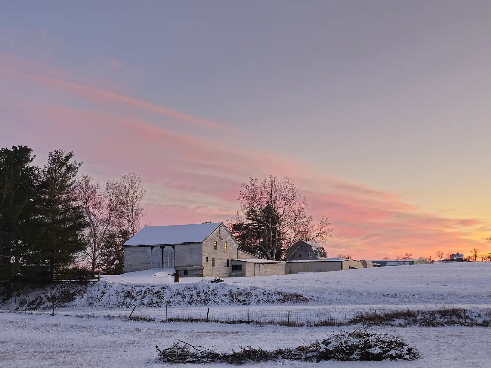 A snowy farm scene featuring a red barn surrounded by snow-covered trees.