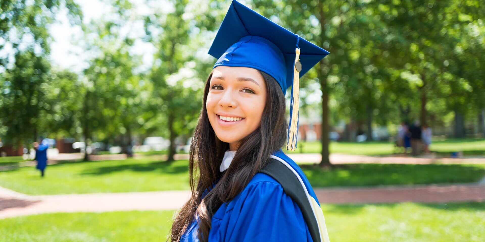 A young woman wearing a graduation gown and cap, symbolizing her academic achievement and success poses outside in a sunny area.