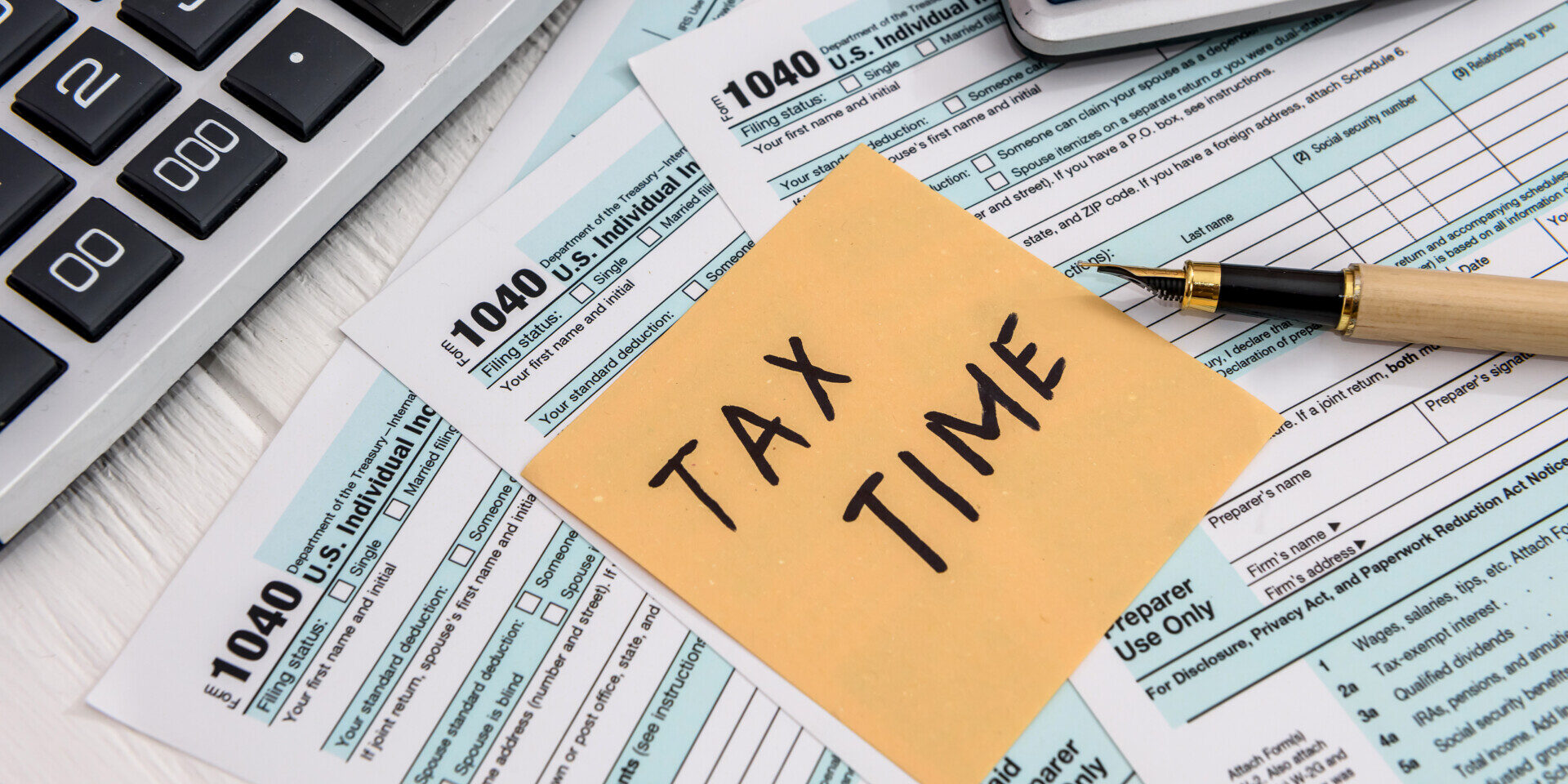 Tax forms and a sticky note that states "tax time" on a table.