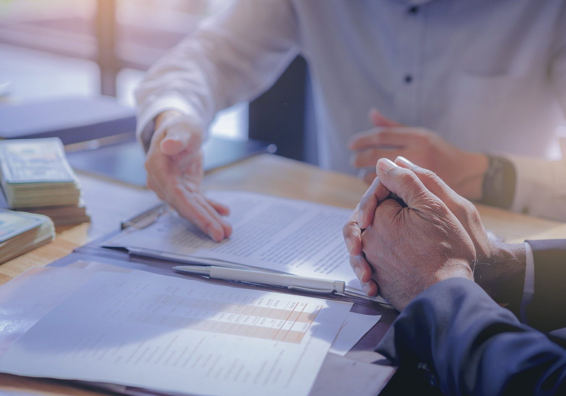 Two business people sitting at a table with papers and money, discussing financial documents and discussing the 5 C's of Credit for small business financing.
