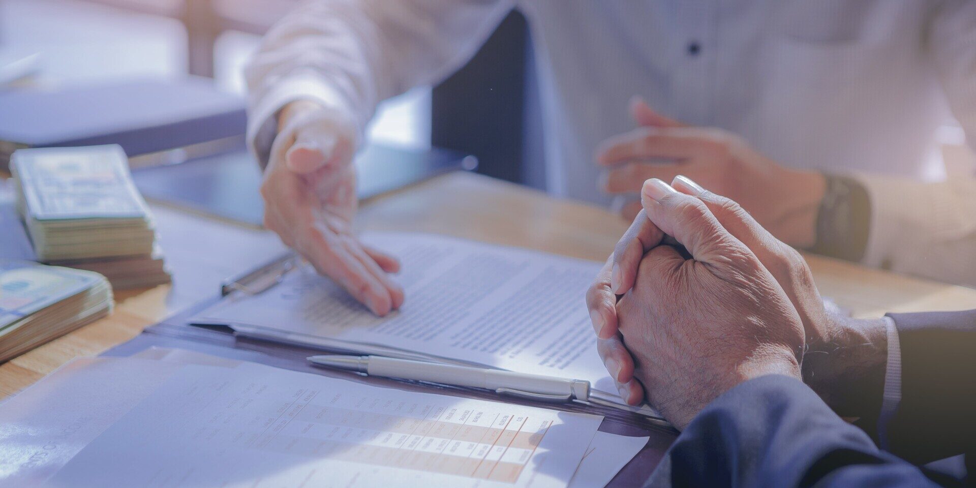 Two business people sitting at a table with papers and money, discussing financial documents and discussing the 5 C's of Credit for small business financing.