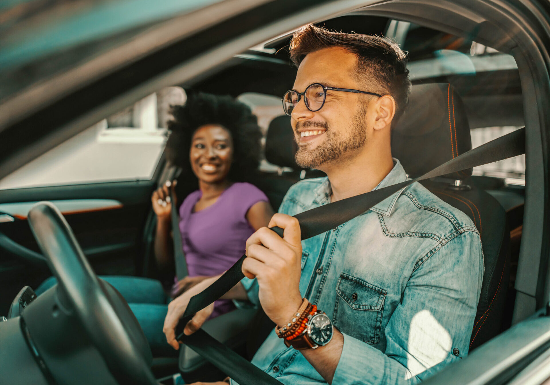 A man and woman sit in the driver and passenger seat of a car, discussing their auto loan options.