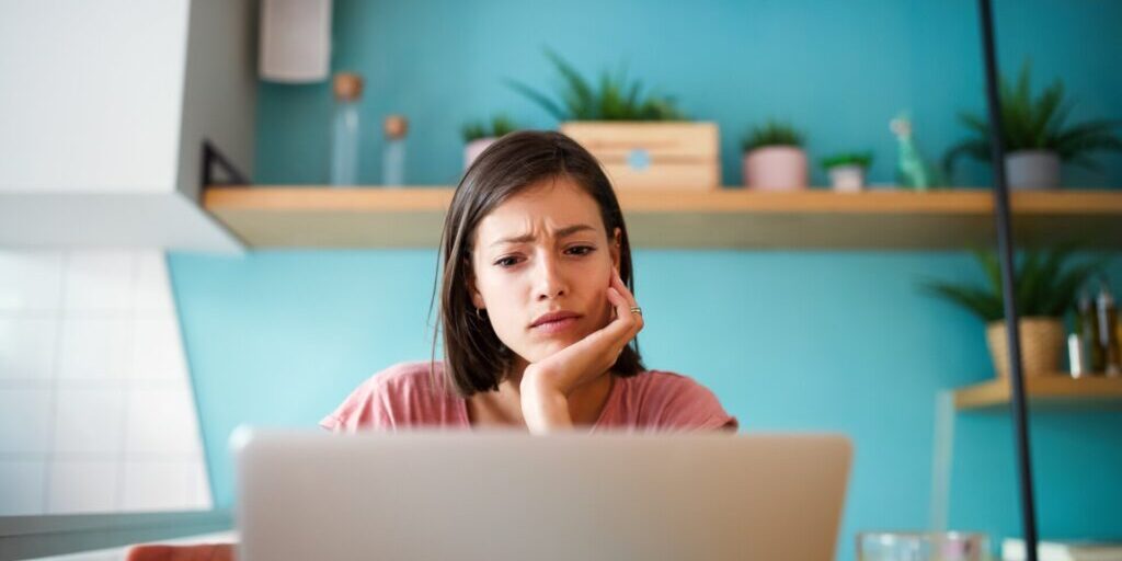 A woman sits at a table with a laptop, looking concerned about a potential data breach.