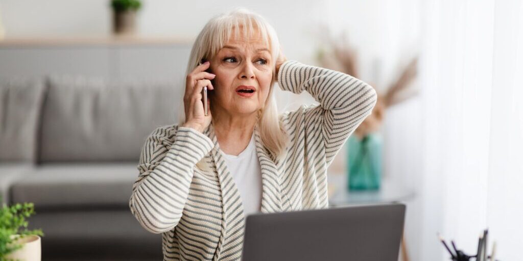 Elderly woman talking on phone at home, potential senior scam or fraud situation.