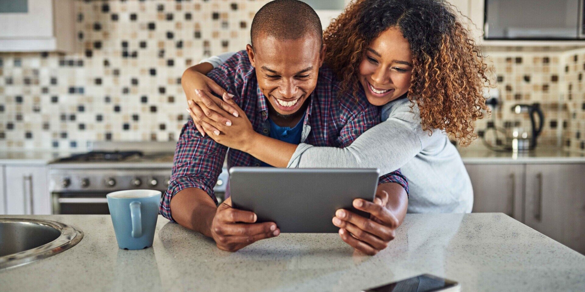 A man and woman in a kitchen are reviewing their online banking details on a tablet together.