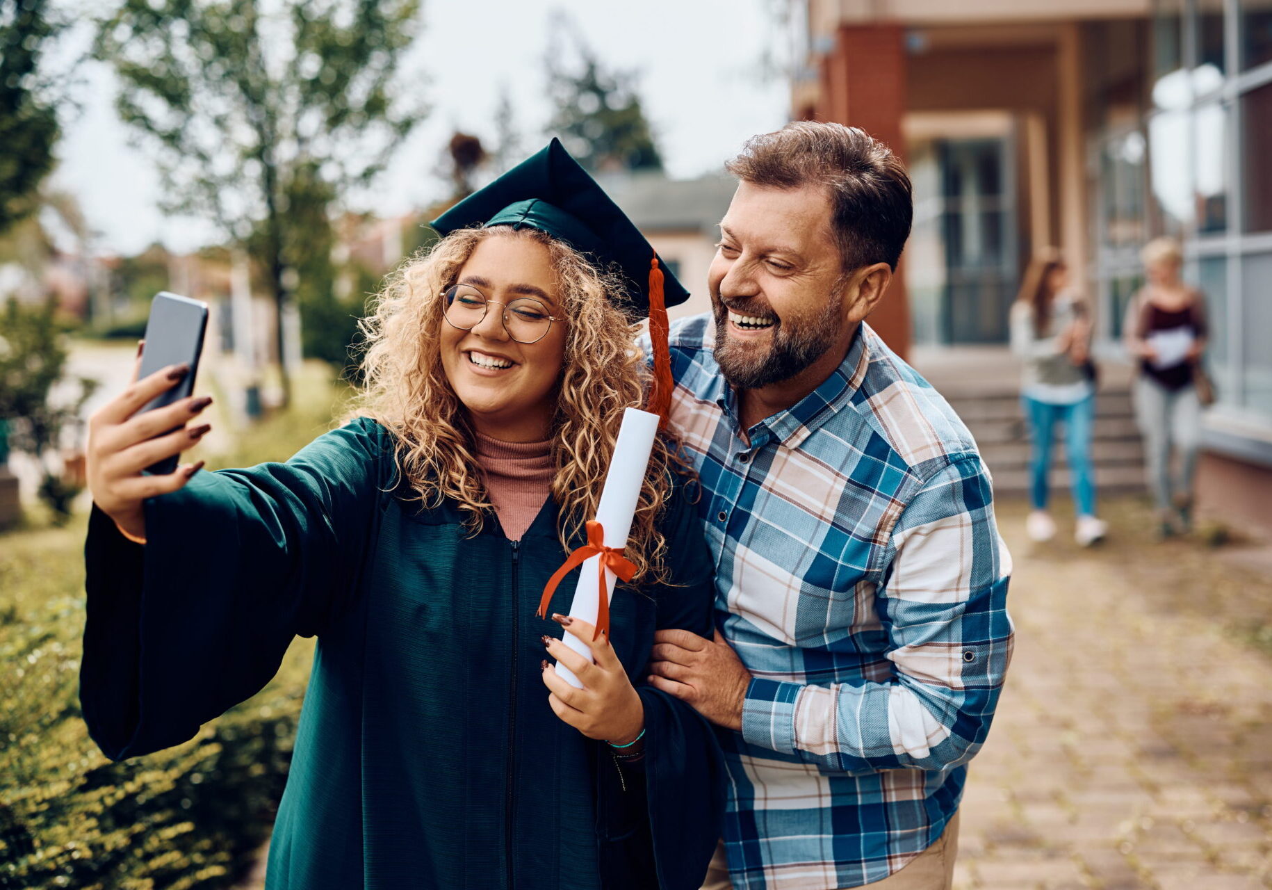 Happy student taking selfie with her father on her graduation day.