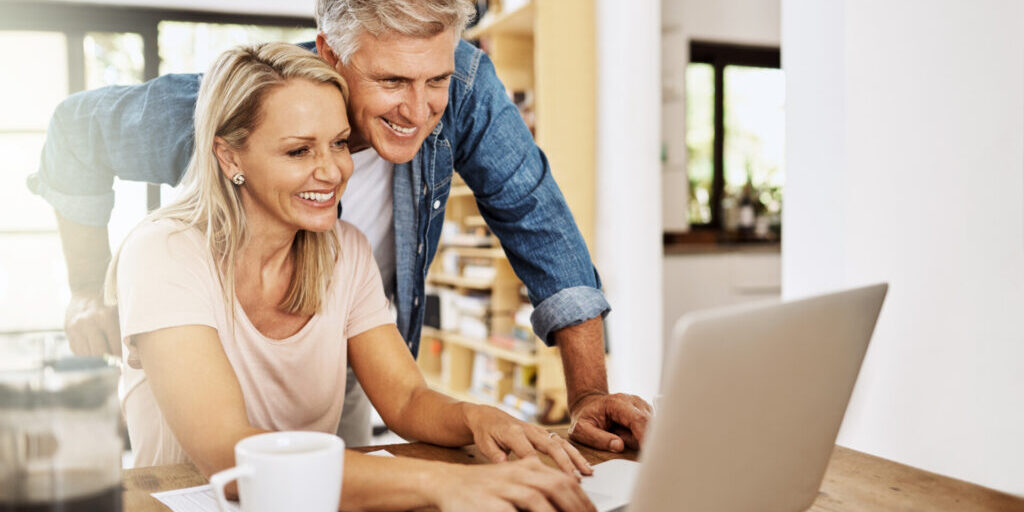 Happy, smiling and mature couple using a laptop together at home. Cheerful Middle aged partners working as a team online.