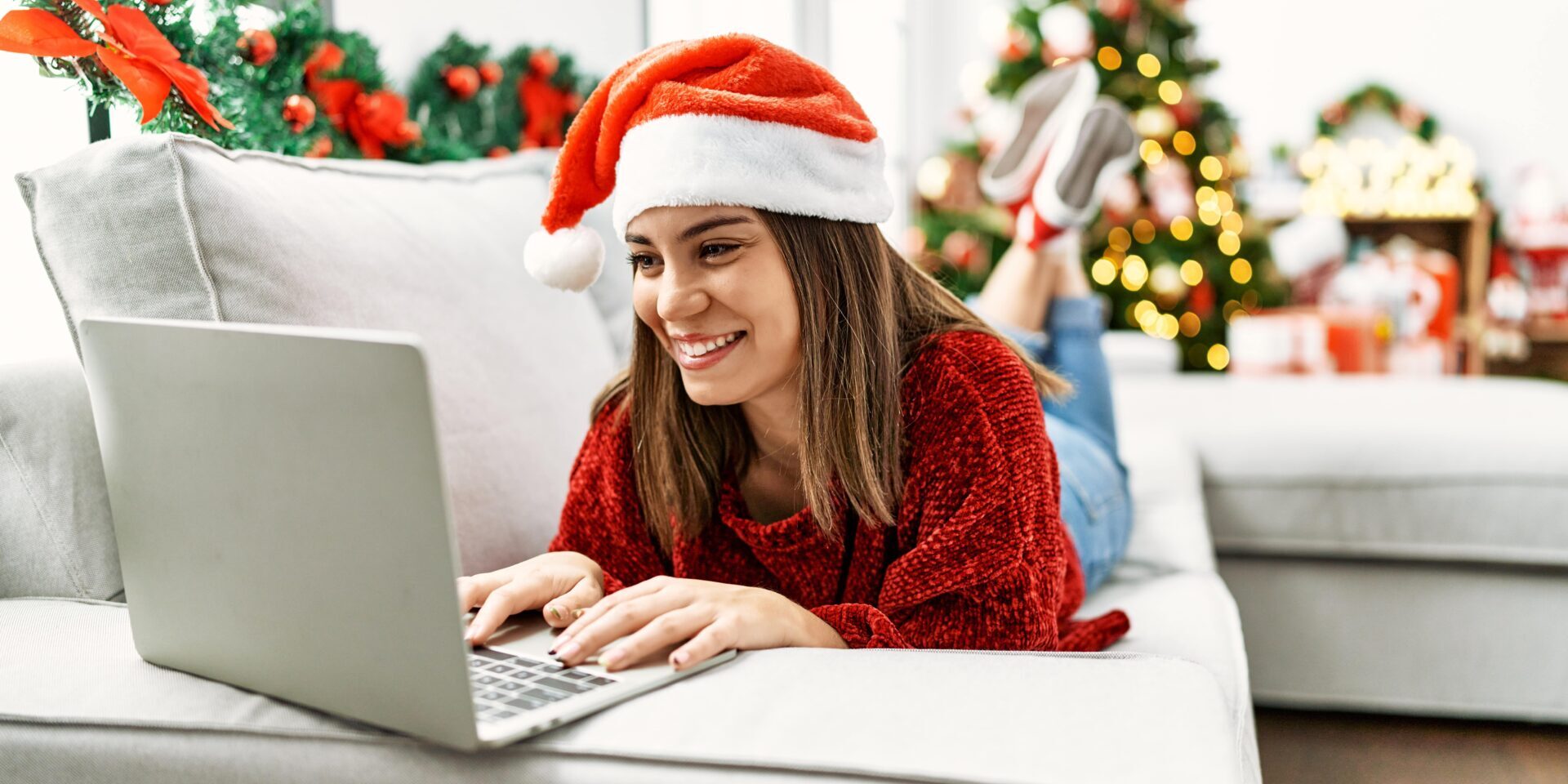 A woman in a festive Santa hat uses her laptop, learning about how to save $1000 for the holidays.