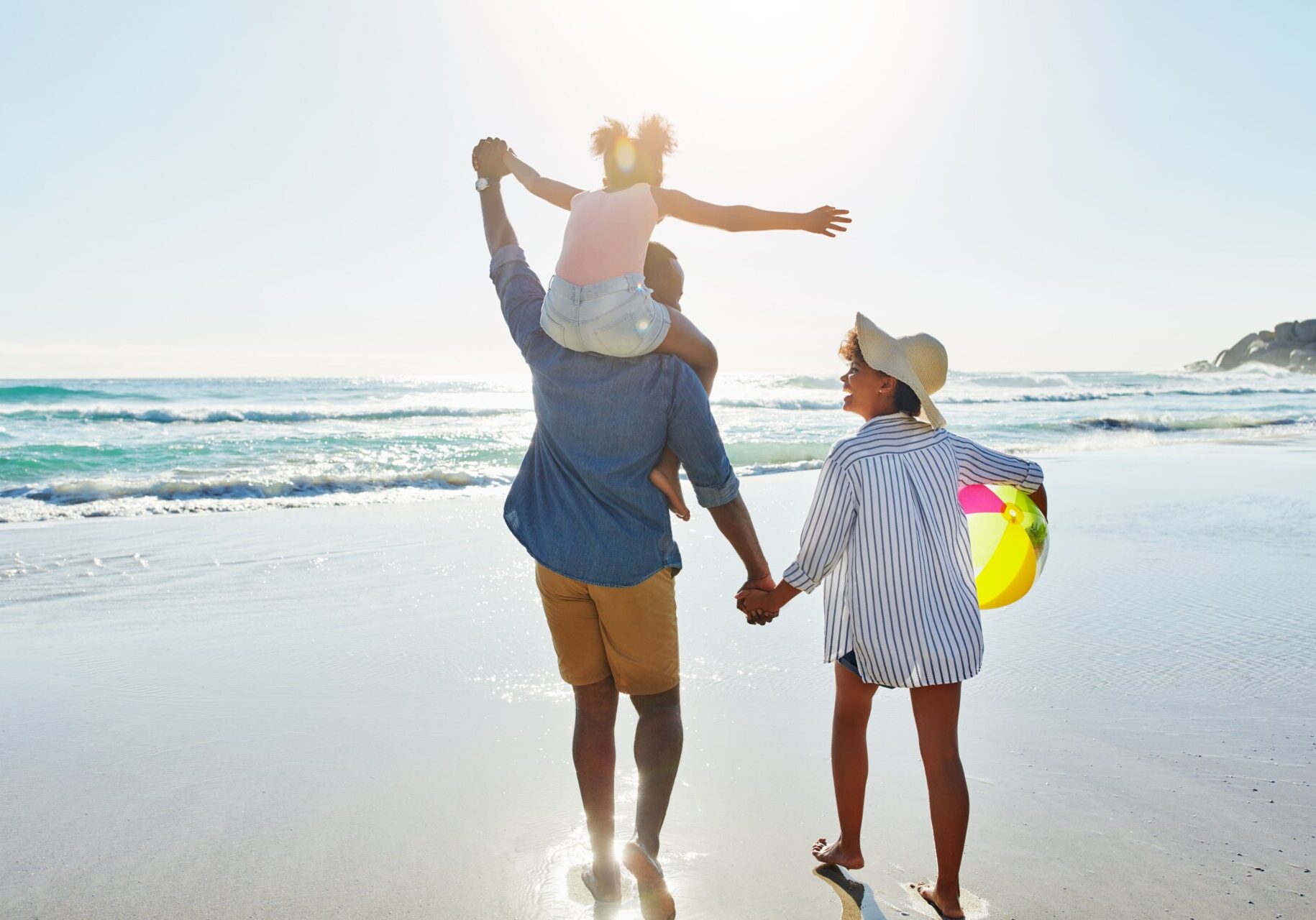 A family enjoying a beach stroll, holding hands, while the sun sets. Thinking of summer savings tips.