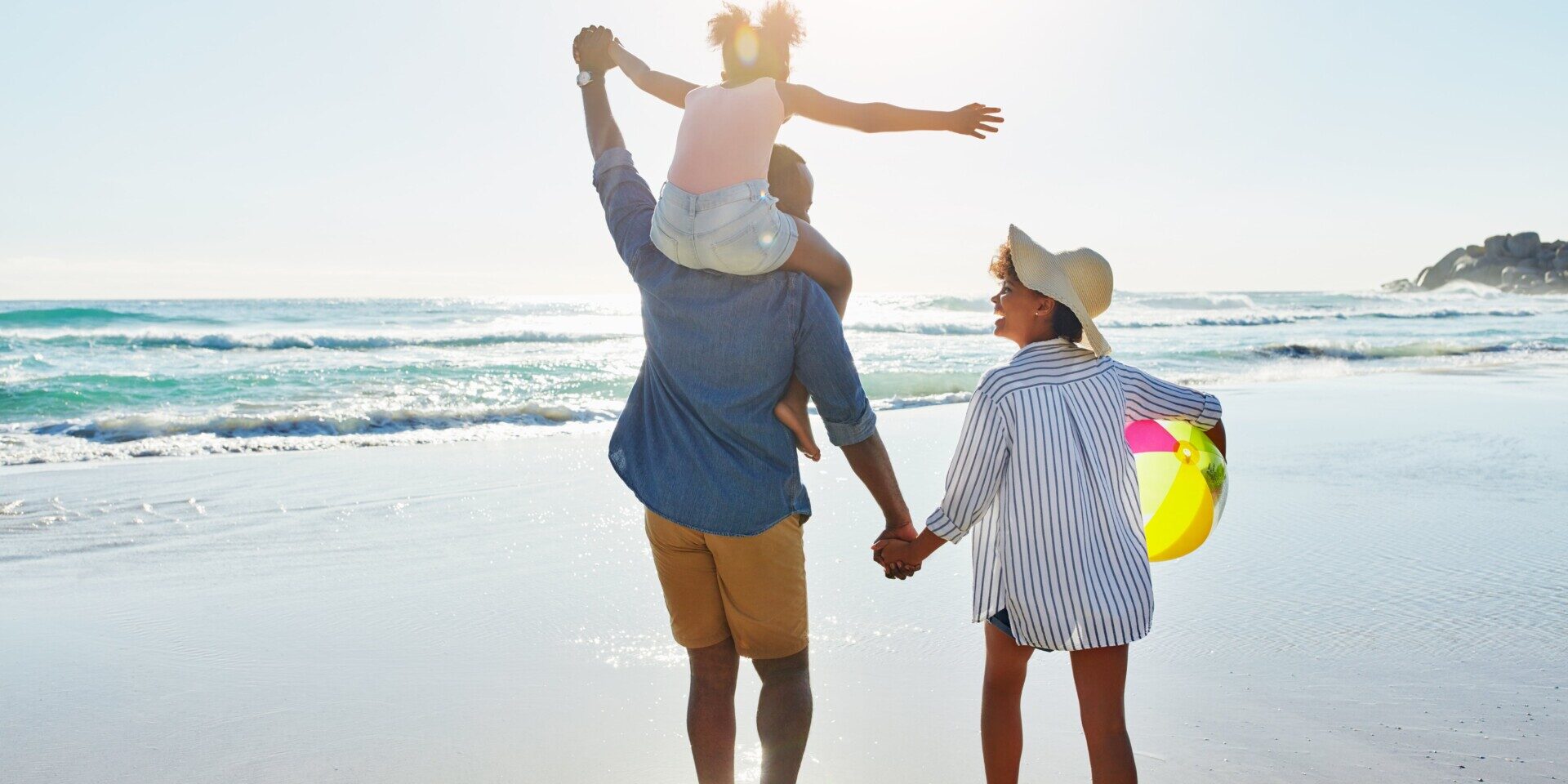 A family enjoying a beach stroll, holding hands, while the sun sets. Thinking of summer savings tips.