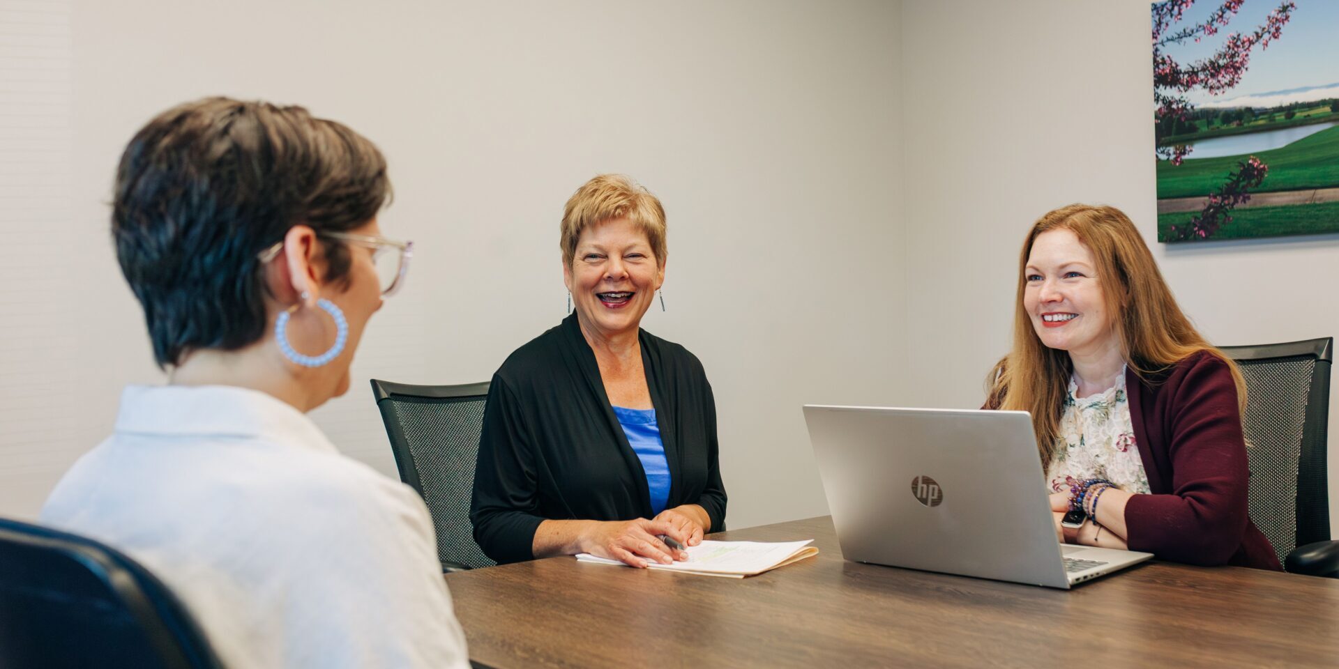 Three women collaborate at a table, discussing financial strategies while using a laptop.