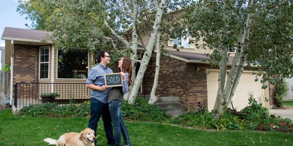 A couple joyfully stands in front of their new home, celebrating their achievement as first-time homebuyers.