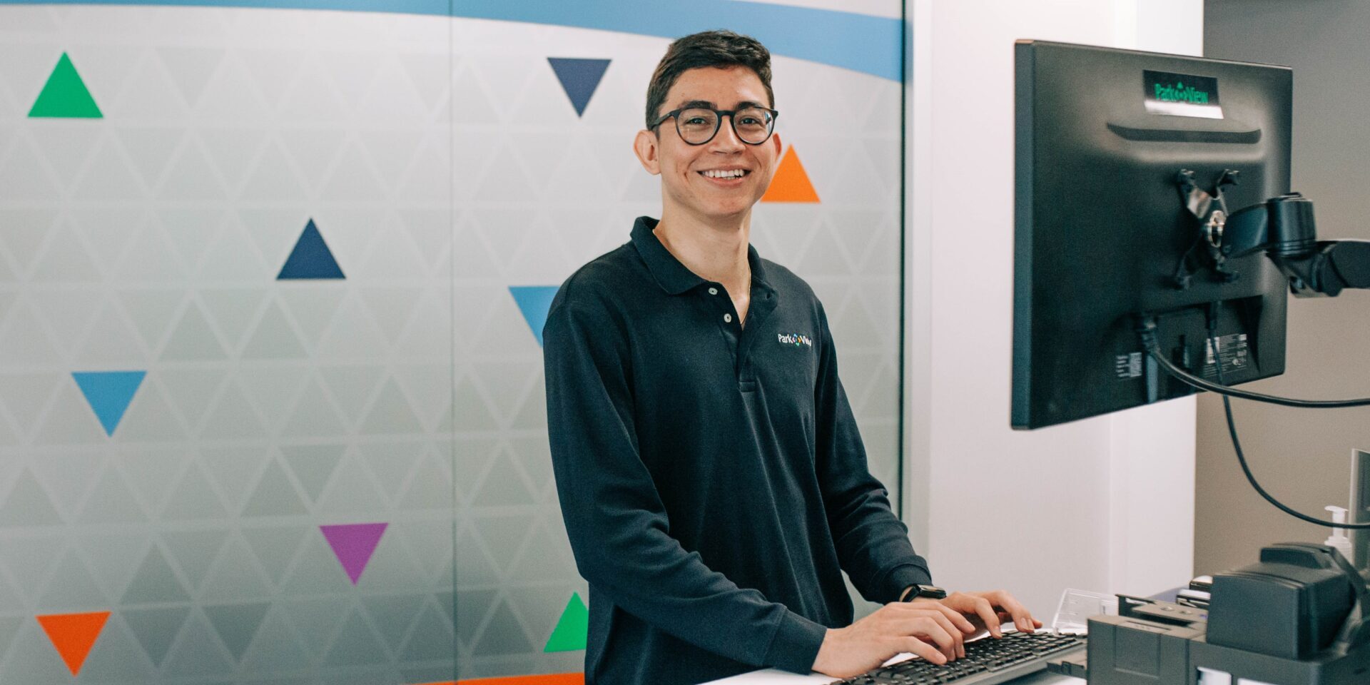 A Park View employee stands at a desk with his hands on the keyboard and smiles at the camera.