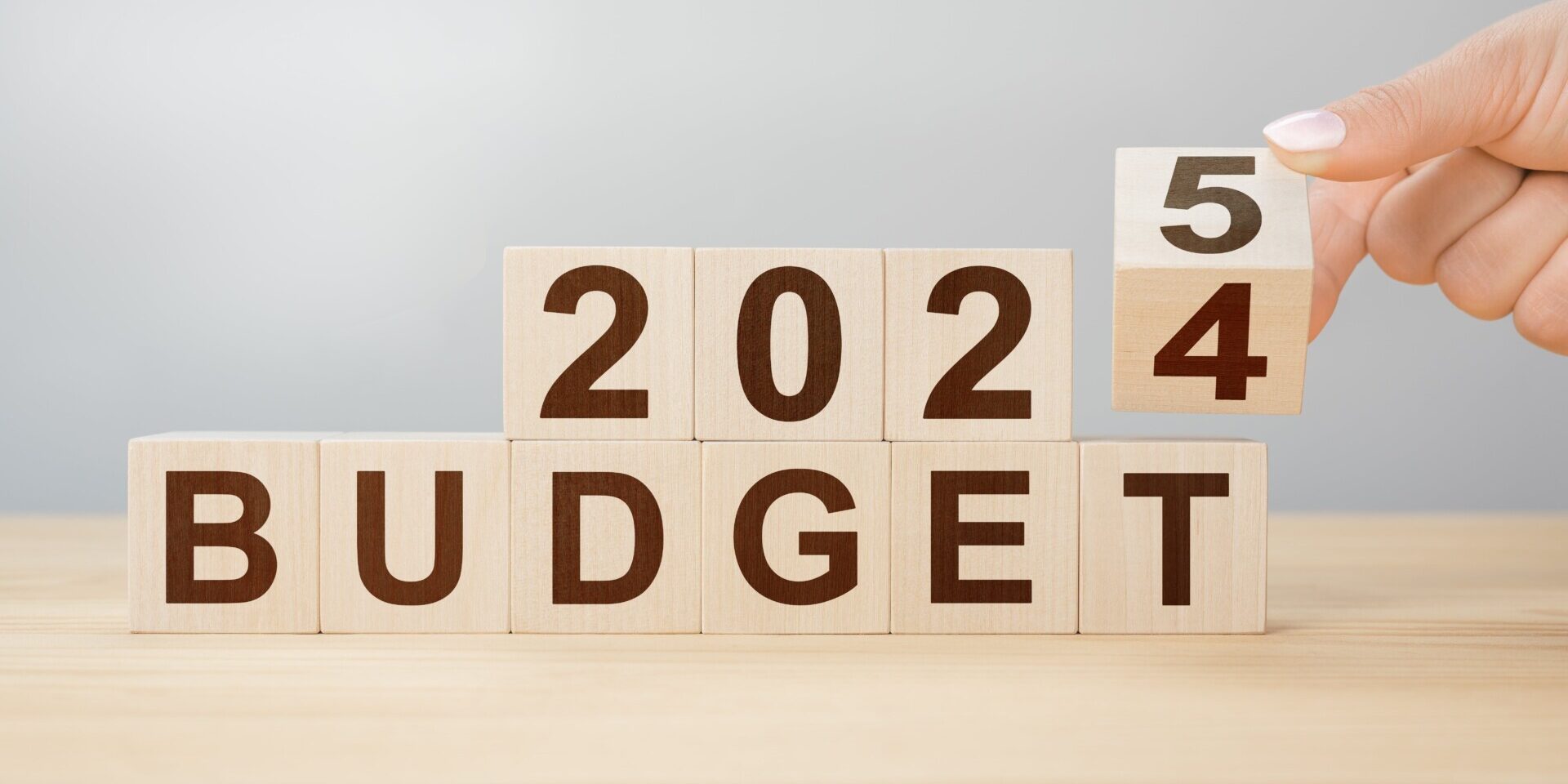 Wooden blocks spell "2024 BUDGET" with a hand changing the 4 to 5, forming "2025 BUDGET." This simple shift symbolizes the transition and offers a reminder on how to stick to a budget all year.