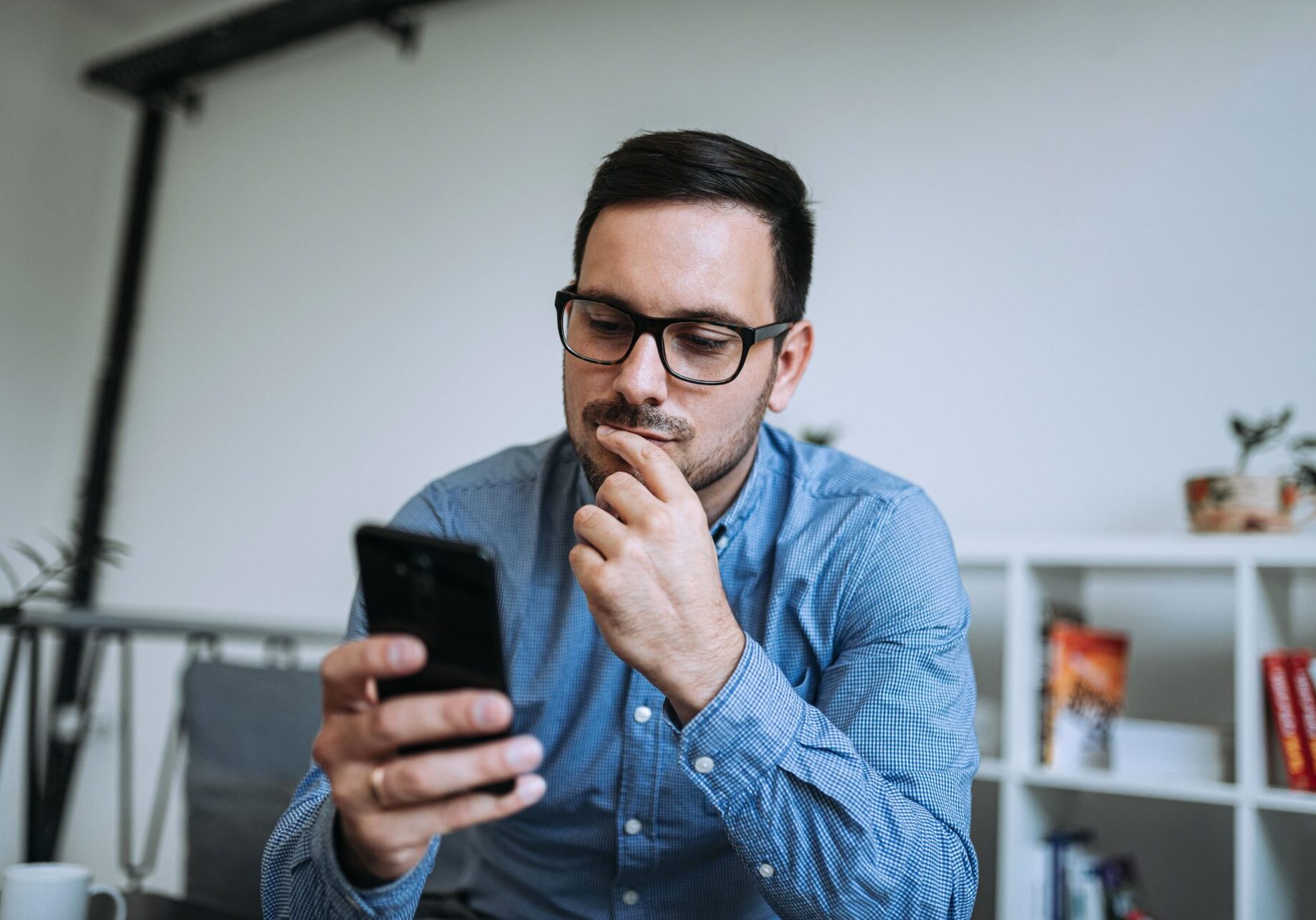 Young thoughtful man looking at mobile phone, concerned about a smishing scam.