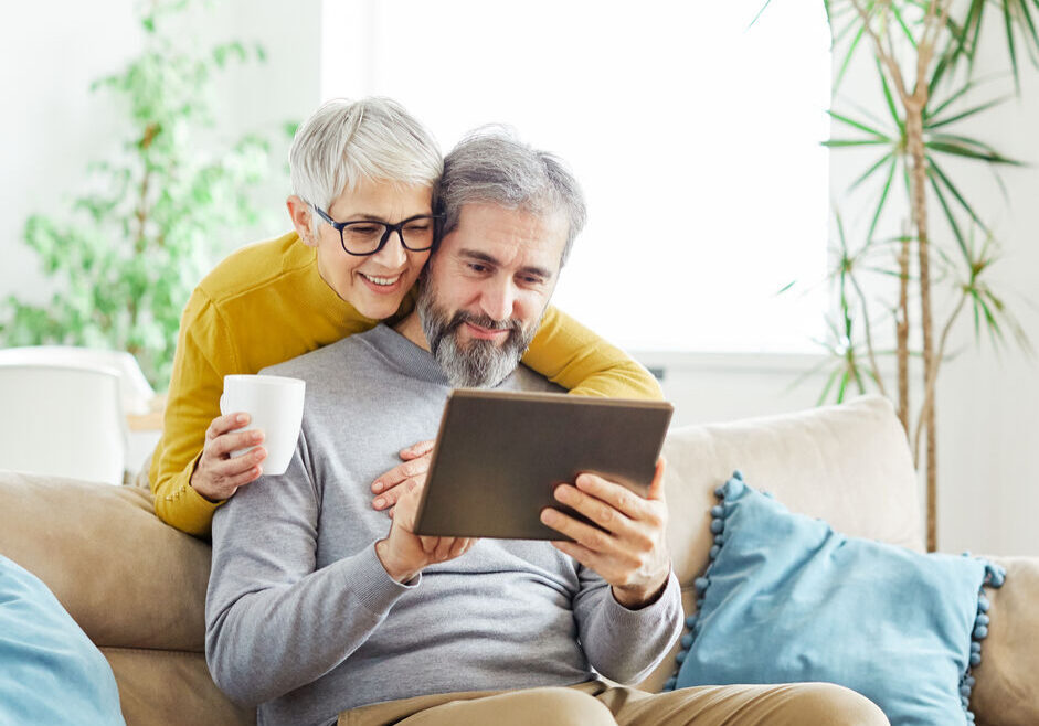 Portrait of a lovely senior mature couple together holding a tablet on sofa at home