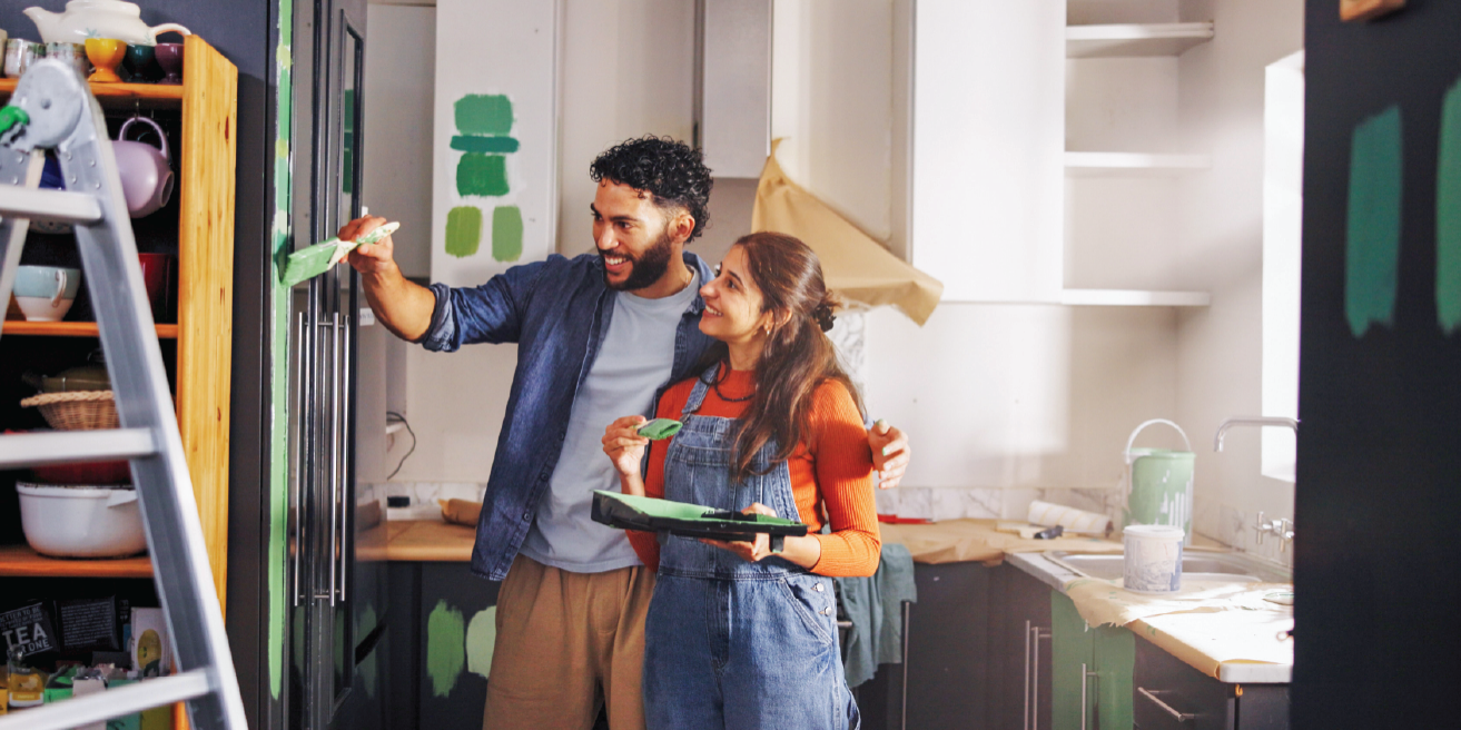 A couple joyfully painting their kitchen walls together, surrounded by paint supplies and a vibrant color palette.