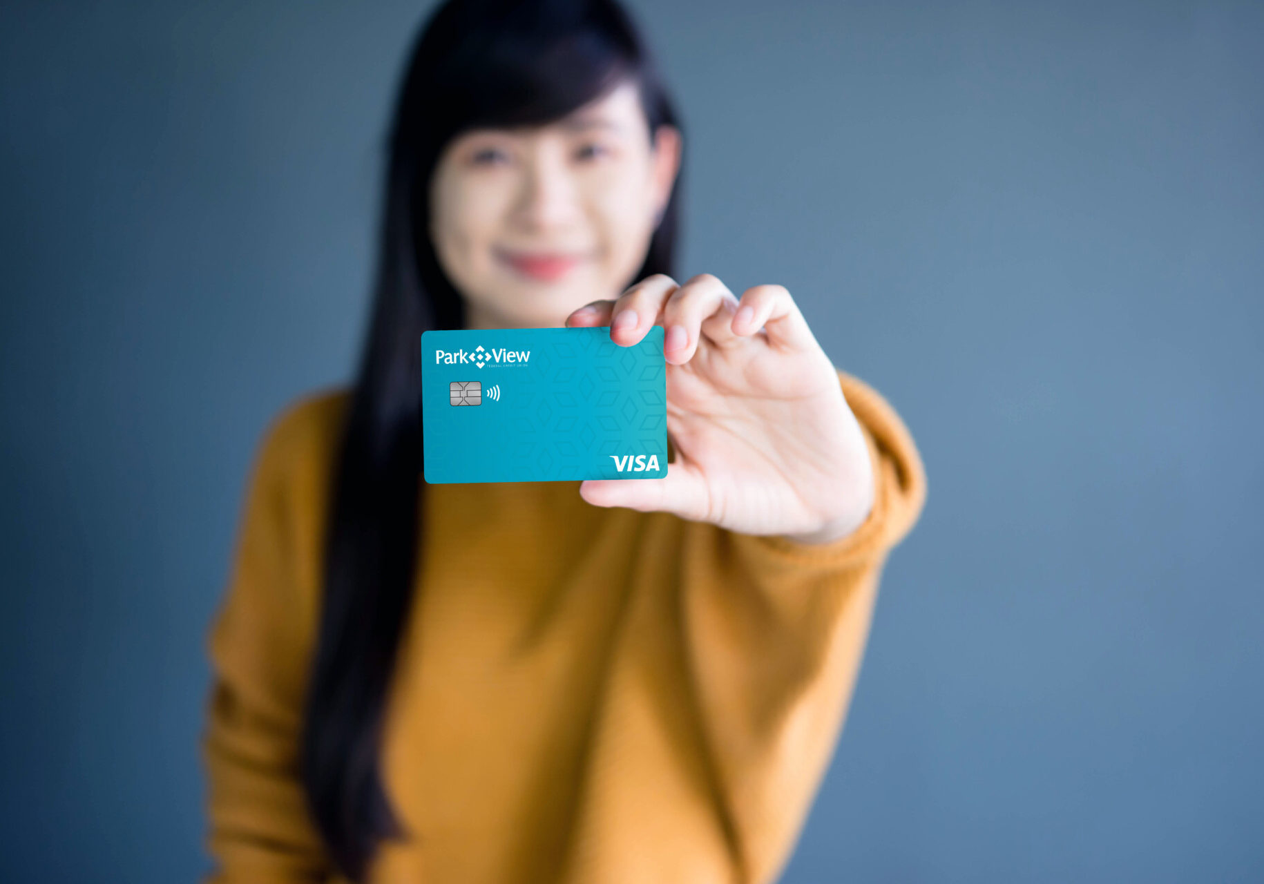 "A young woman holding a Park View Visa credit card, smiling and presenting it towards the camera.