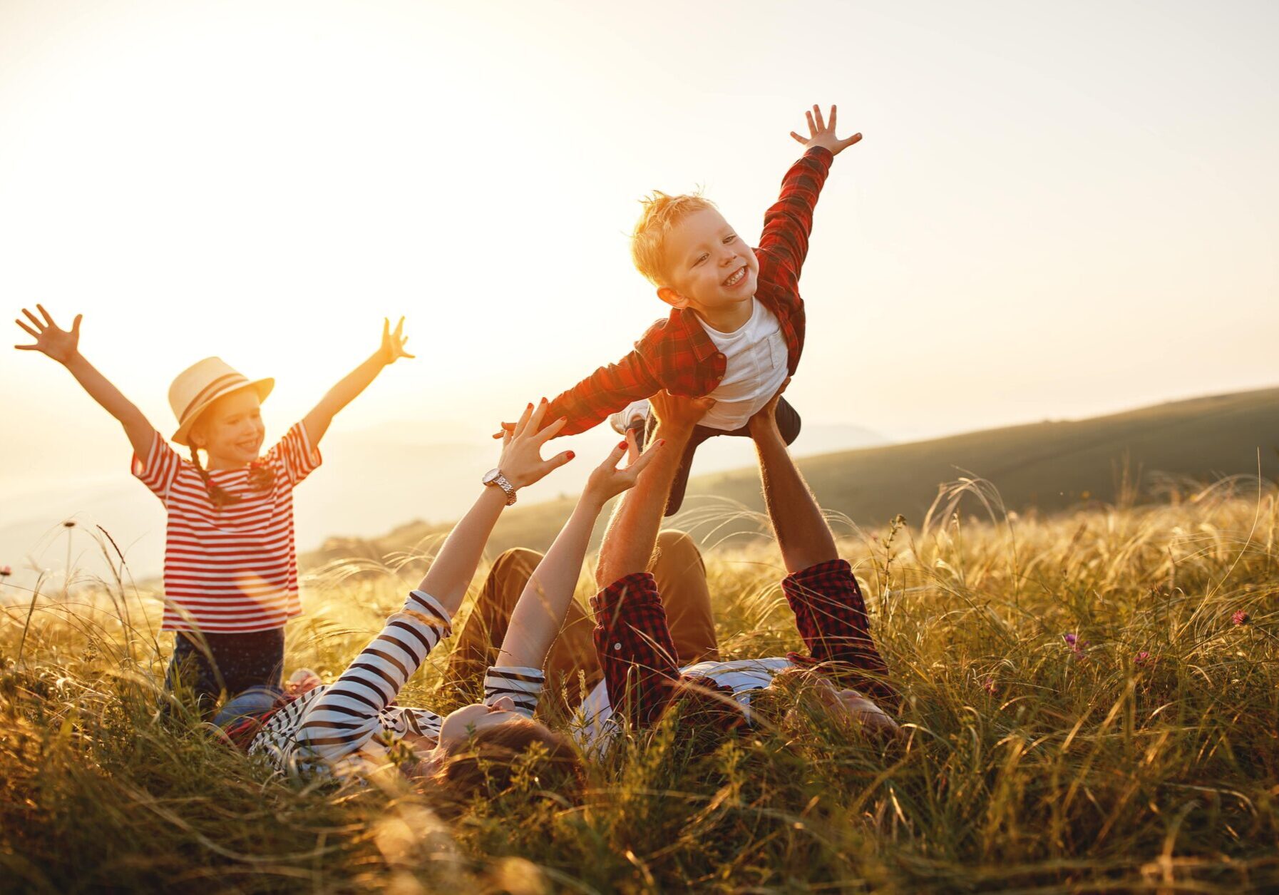 A family laughs and plays on the grass, creating happy memories at sunset.