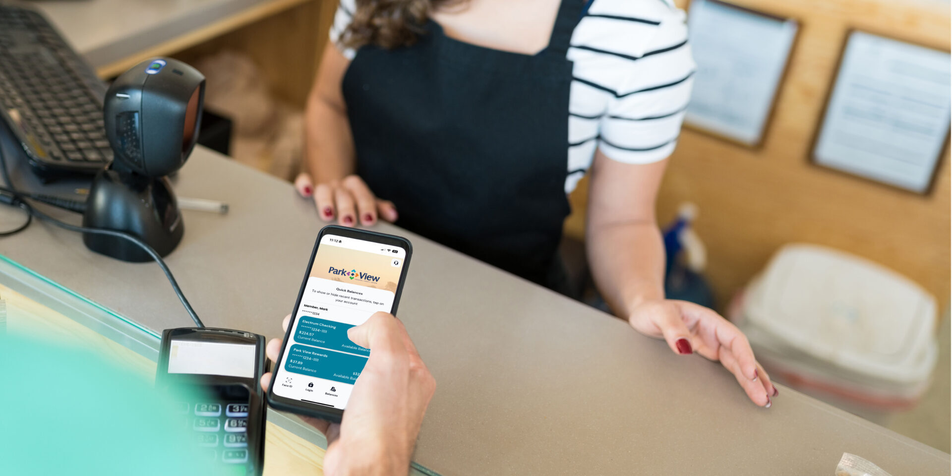 A man's hand holding a phone at a grocery store check out, using Park View's quick balance feature to check his balance.