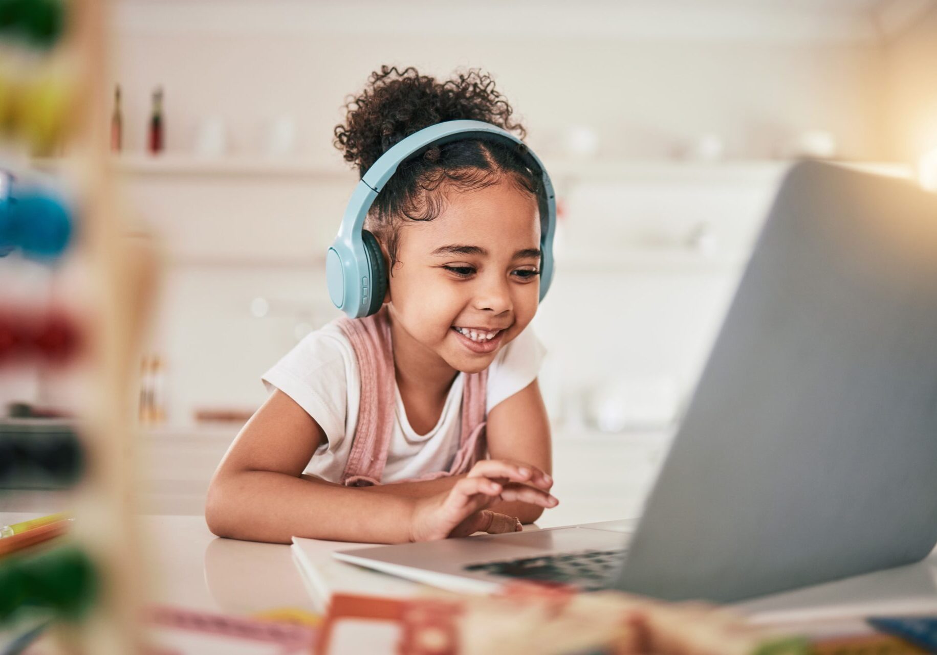 A cheerful girl wearing headphones uses a laptop, happily exploring online while staying safe from potential scams.